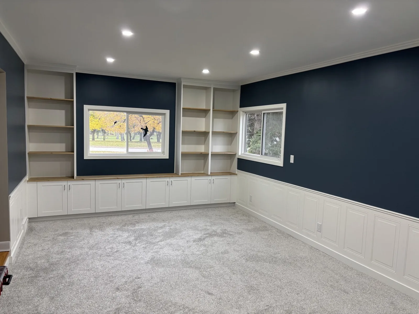Navy-walled family room with white built-in shelving and cabinets, wainscot panelling and new carpet