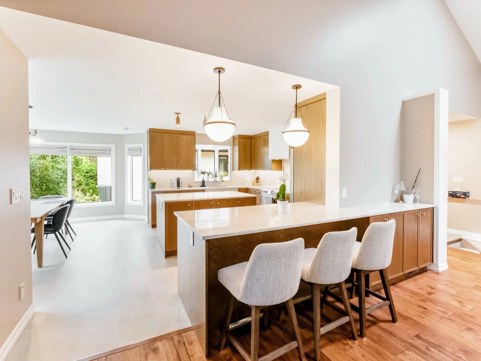 Oak kitchen with a seated peninsula and island under globe pendants, open to a bright dining area