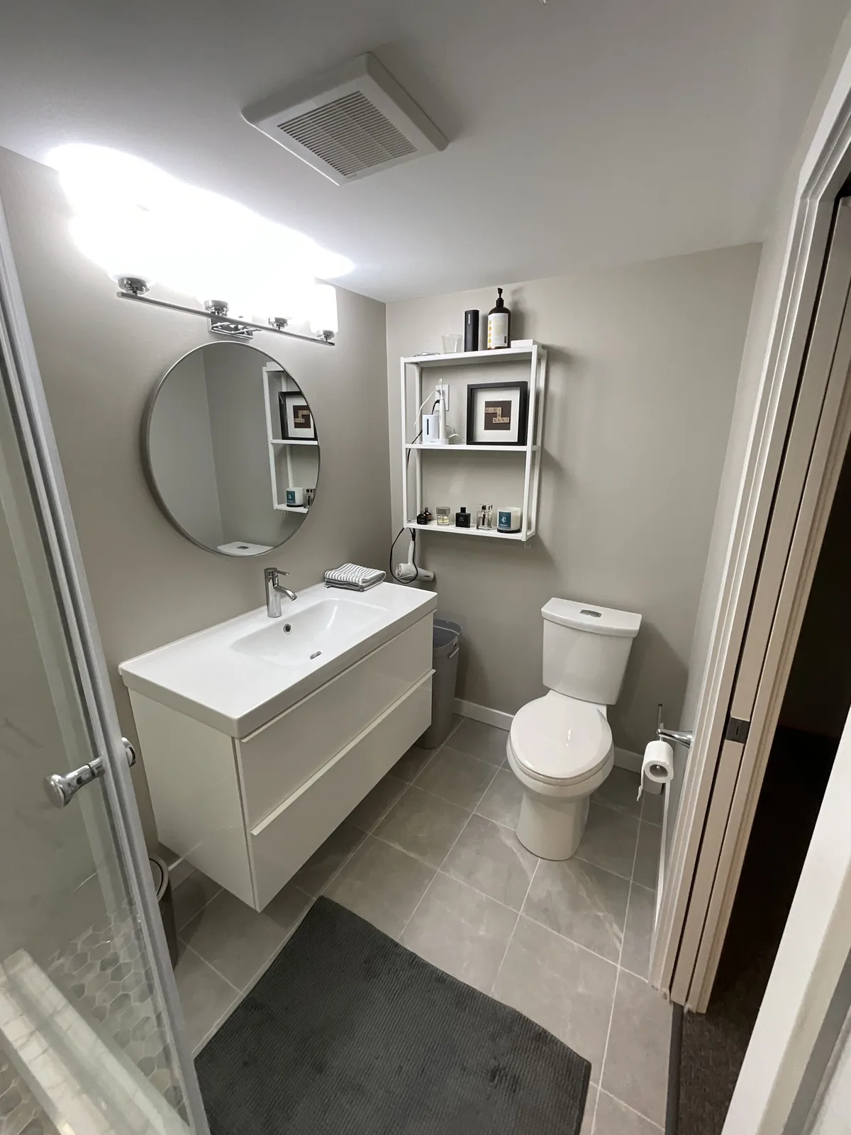 Vanity, mirror and toilet along the wall, shelving above