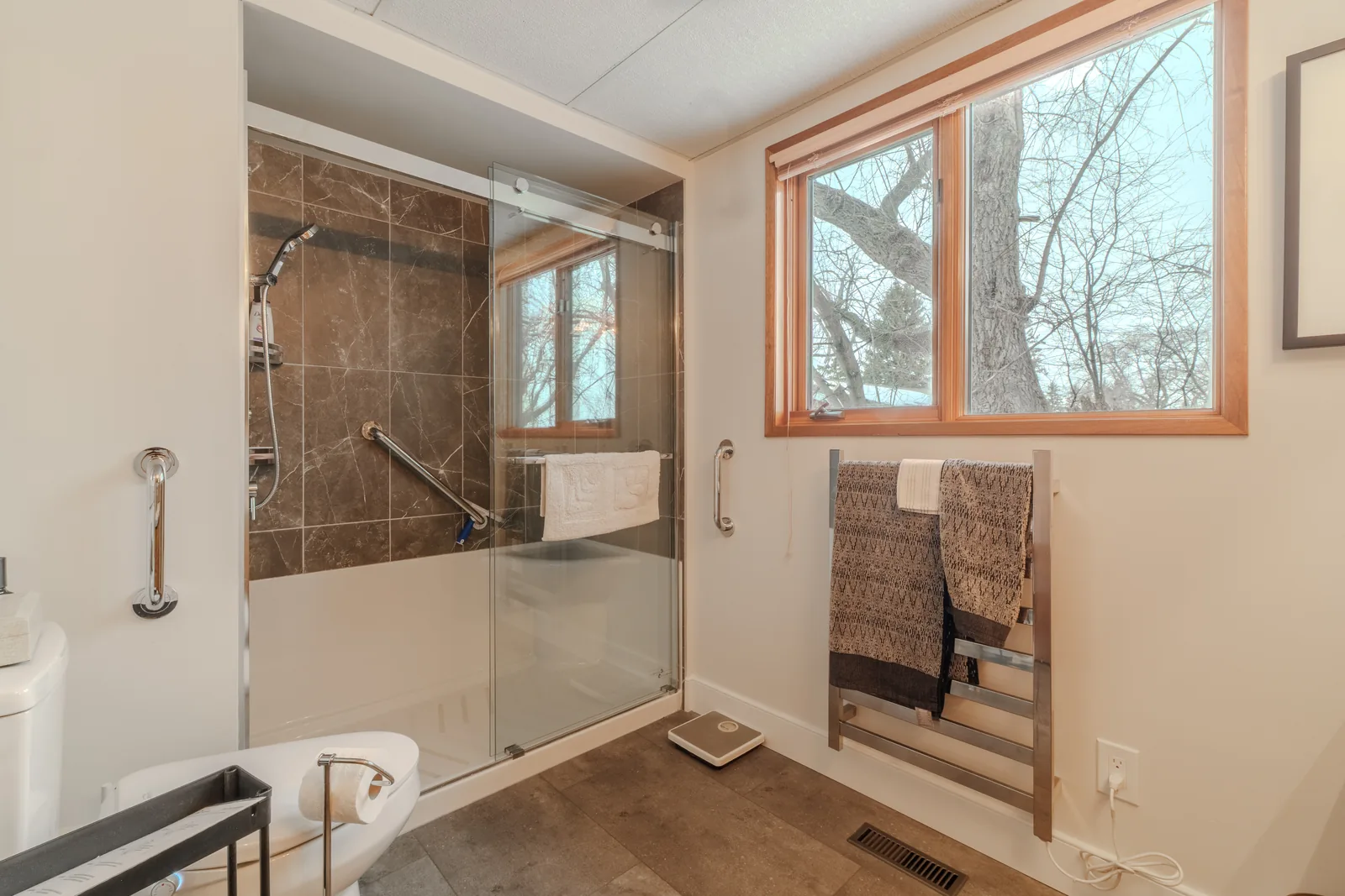 Curbless glass shower with a grab rail, window looking into the trees