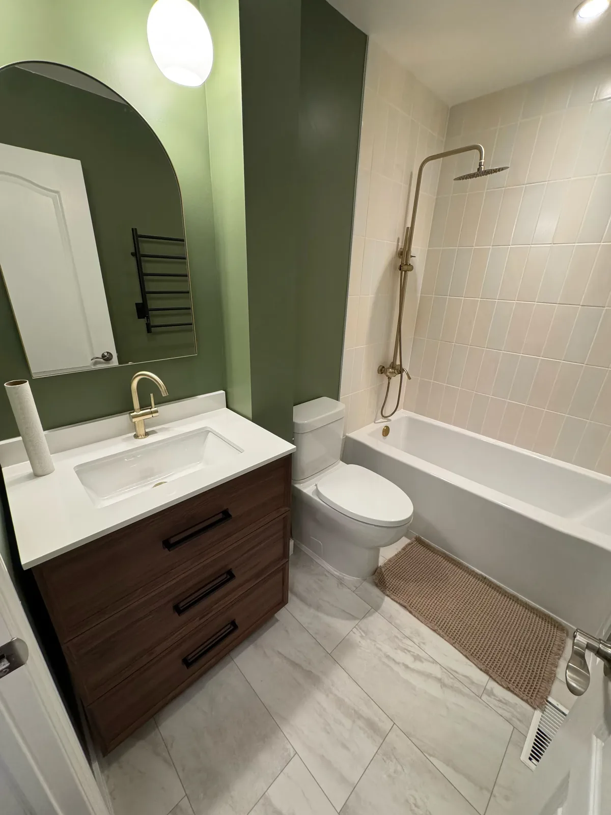 Olive-green bathroom with a walnut vanity, arched mirror and brass fittings