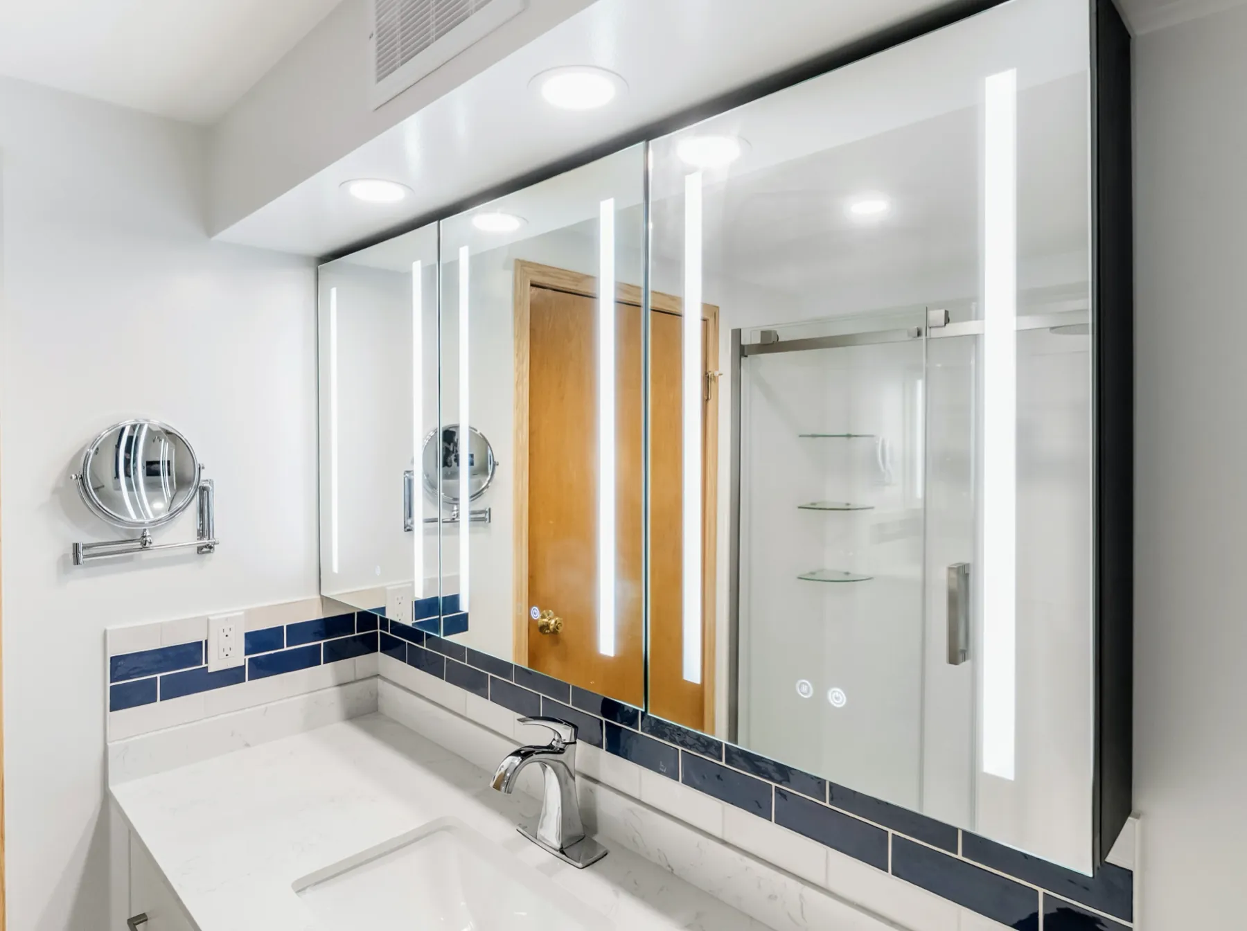 The lit mirror cabinet above the quartz counter
