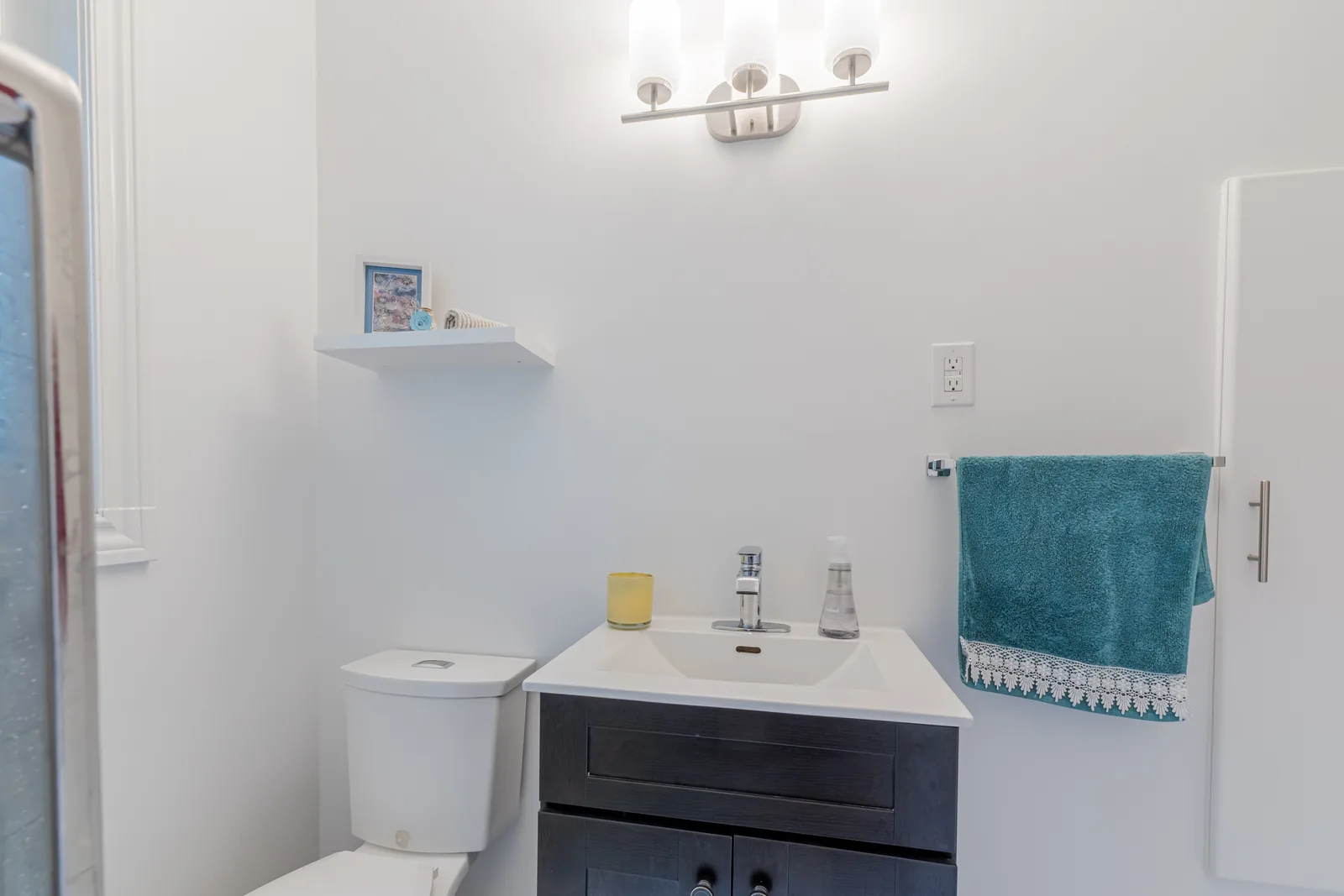 The vanity under its sconce, toilet and shelf alongside