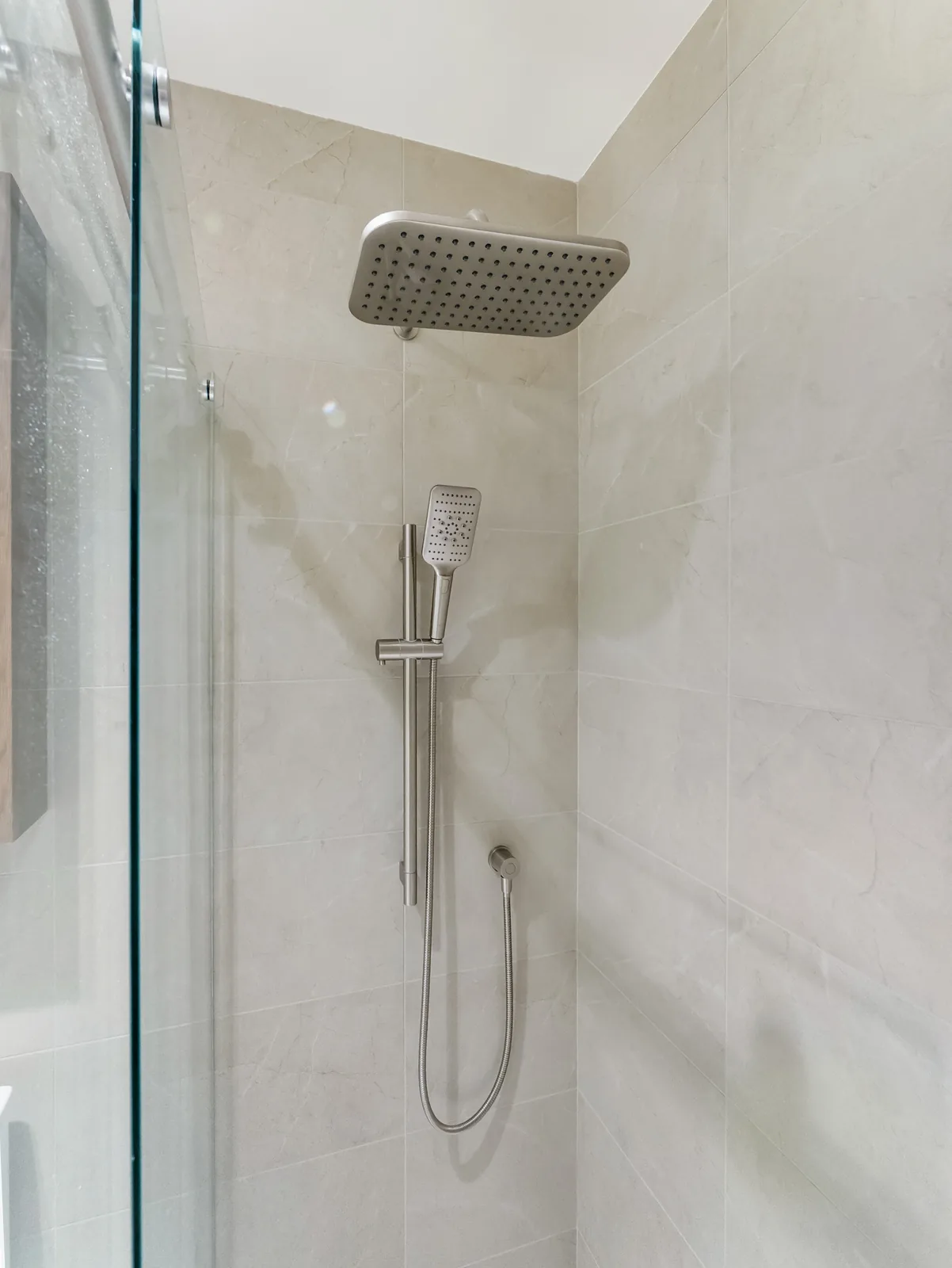 Rain head and hand shower on the tiled wall behind the glass