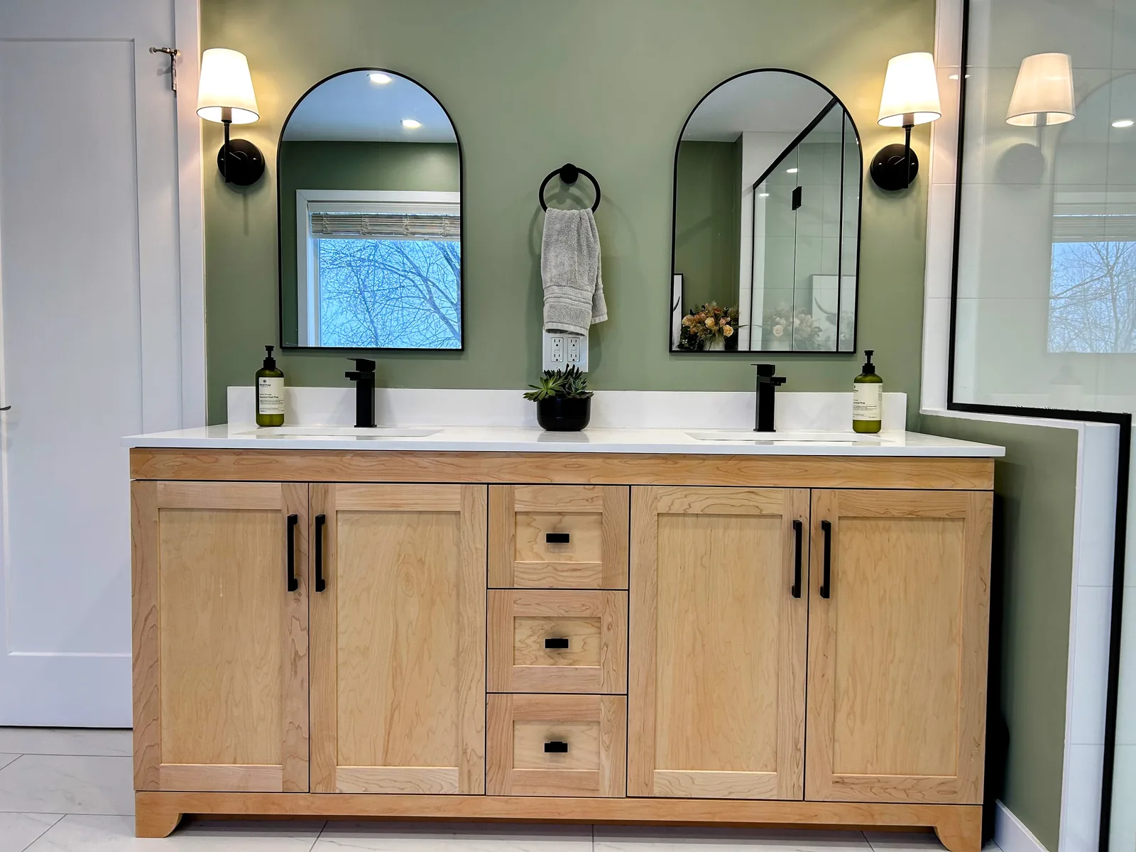 Double vanity in light oak under twin arched mirrors, black sconces between them