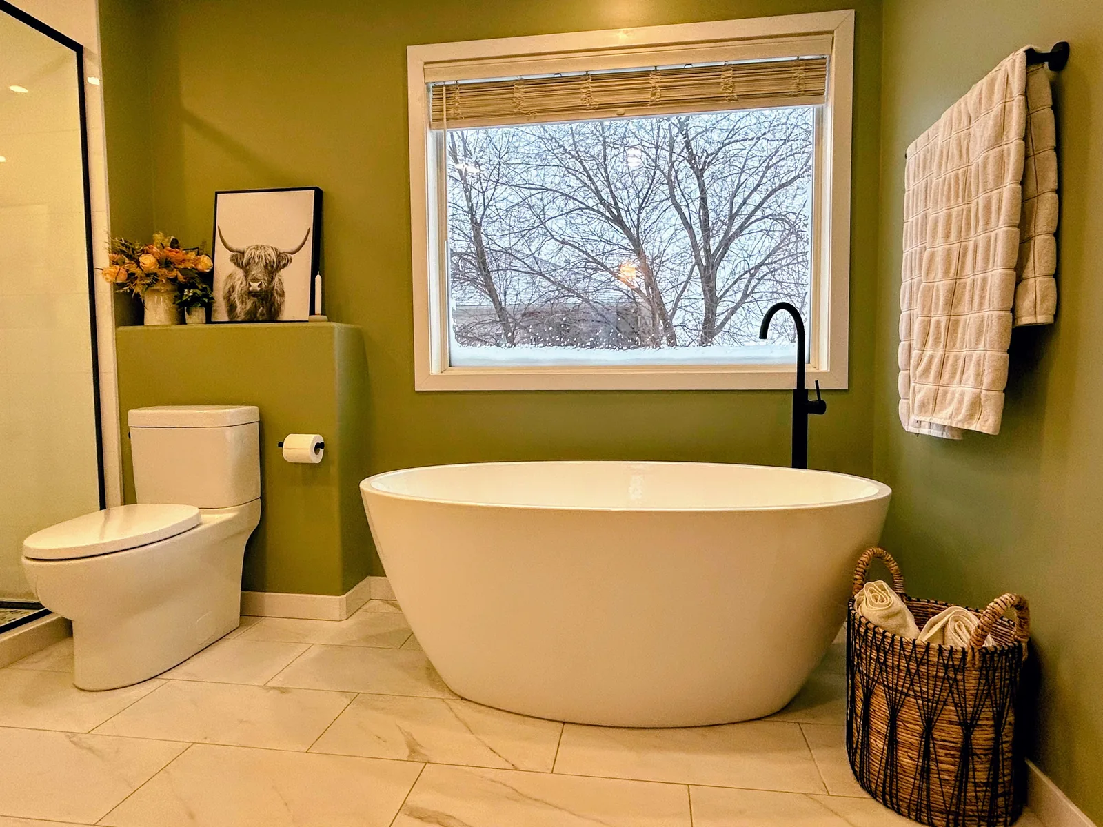 Freestanding soaker tub set at the picture window, olive walls around it