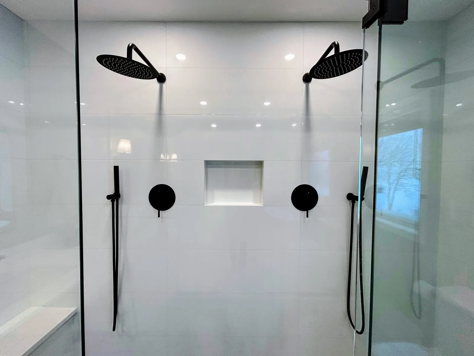 Twin rain heads and hand showers on the white slab-tiled shower wall