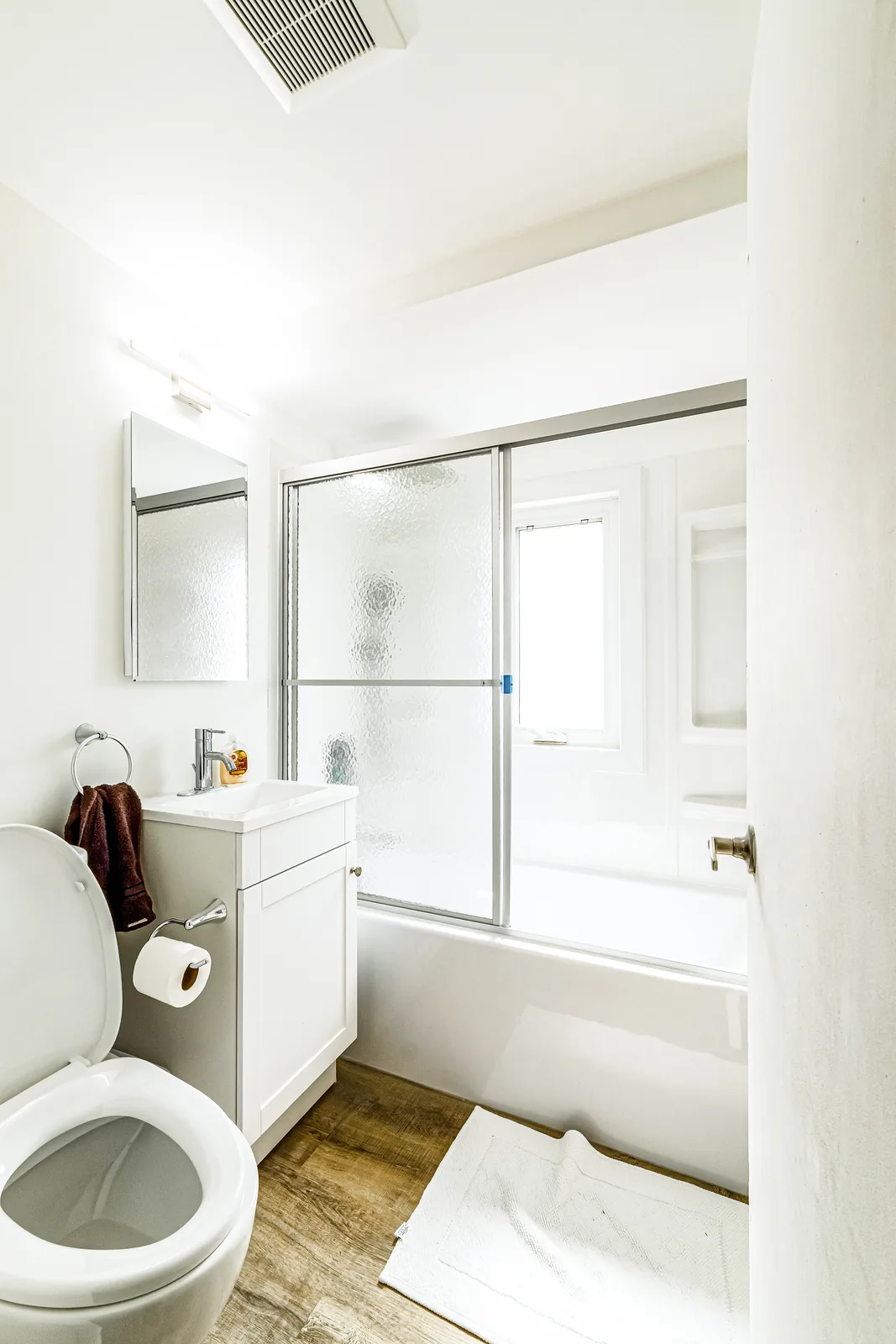 Bathroom with a white tub-shower and plank flooring run through