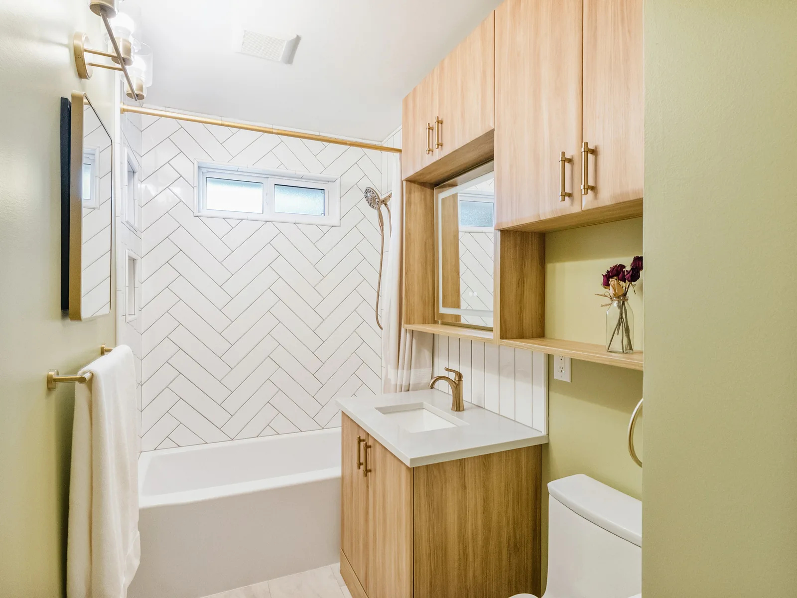 Sage-green bathroom with an oak vanity, herringbone-tiled tub wall and brass fittings