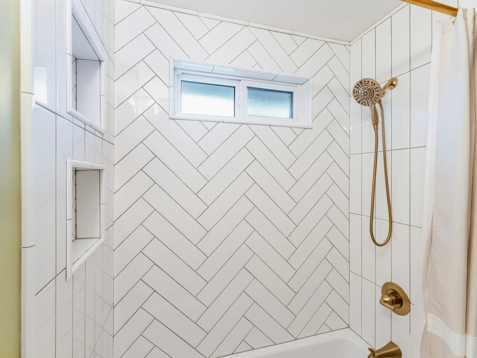 White herringbone tile running up the shower wall to the window