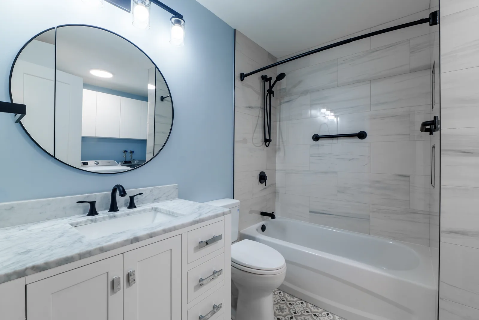 Vanity and mirror from the tub end, black fittings on marble-veined stone