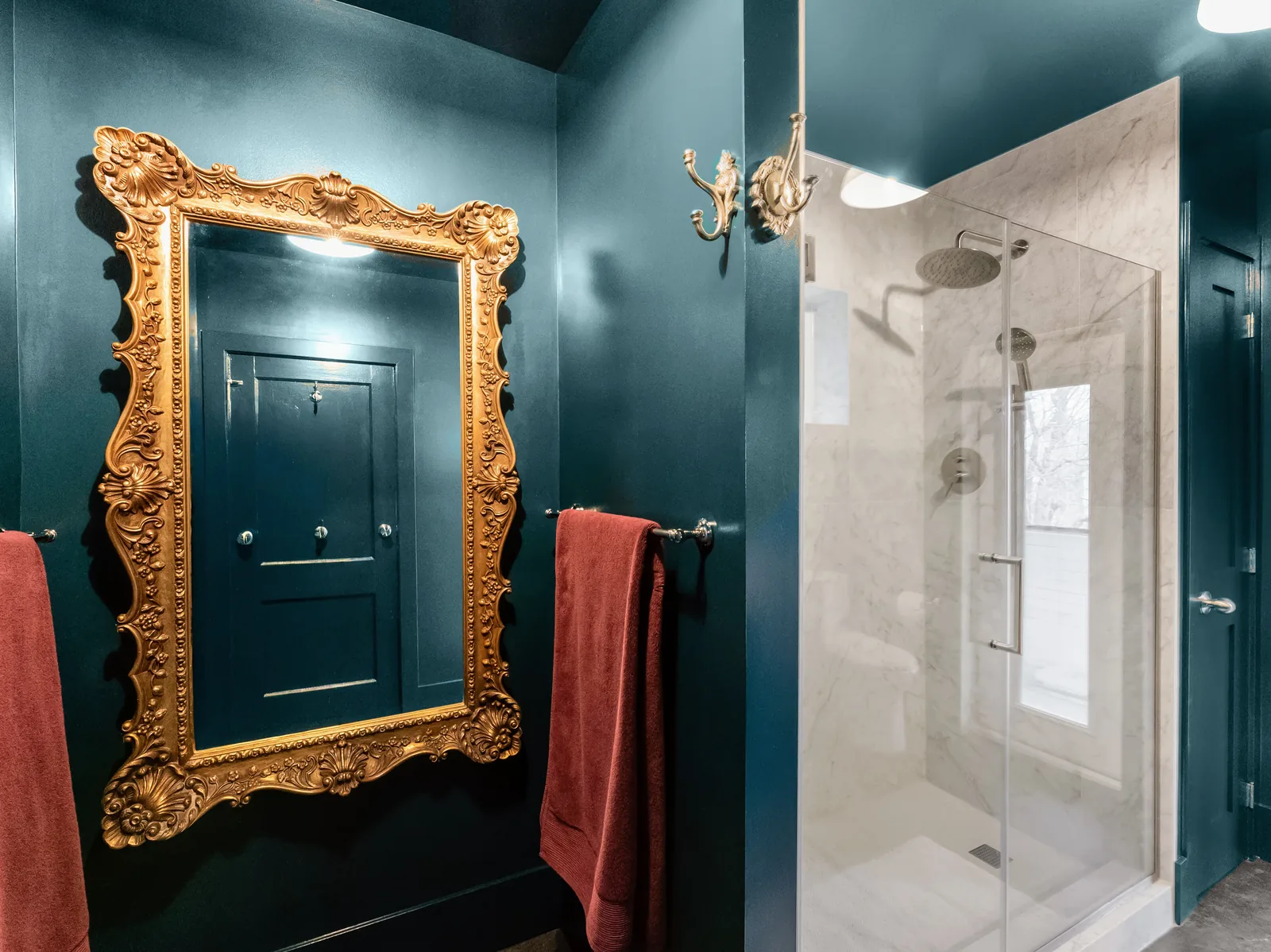 Ornate gilt mirror hung on the teal wall opposite the shower