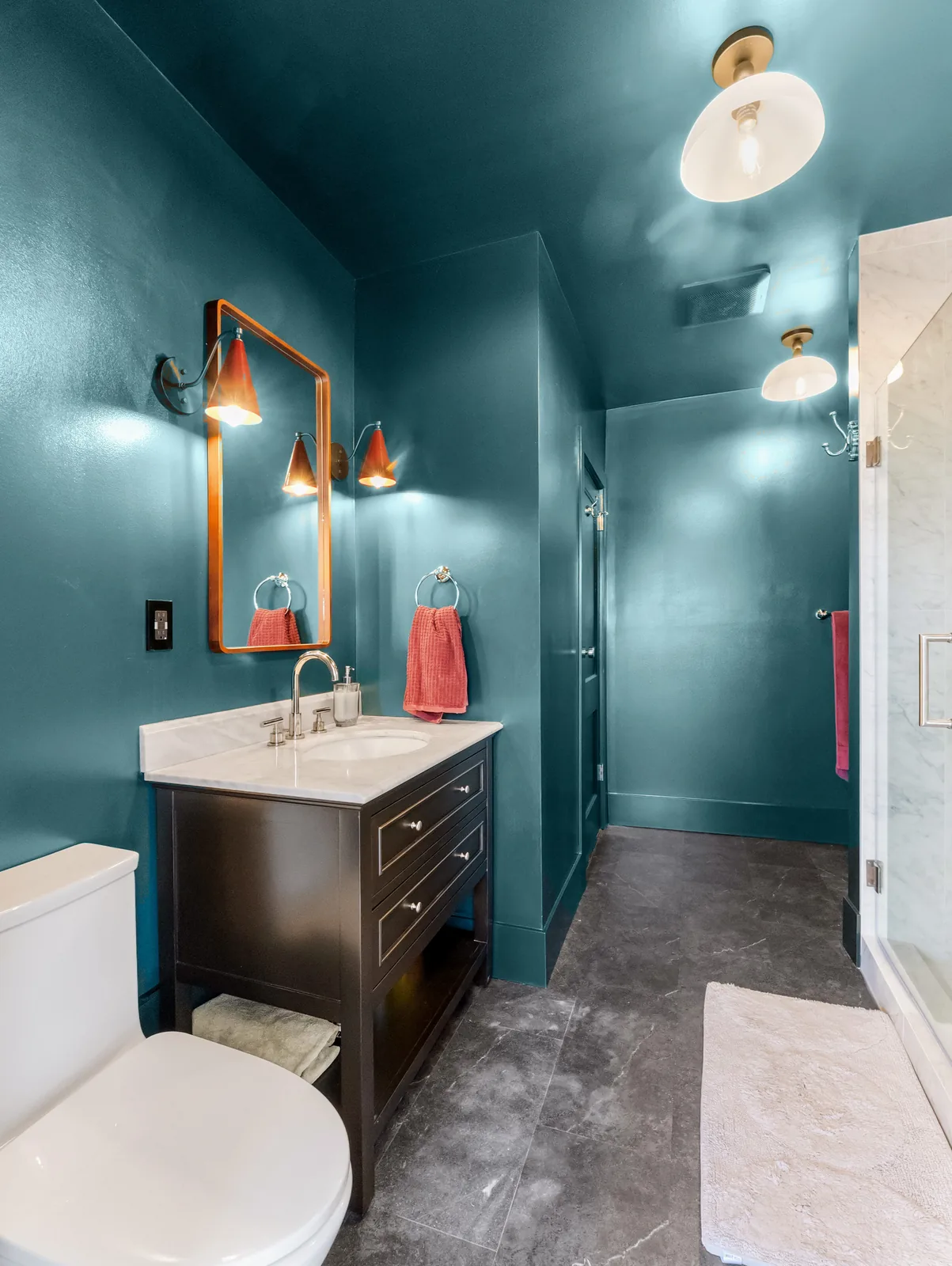 Looking back to the door past the vanity, sconces lit either side of the mirror
