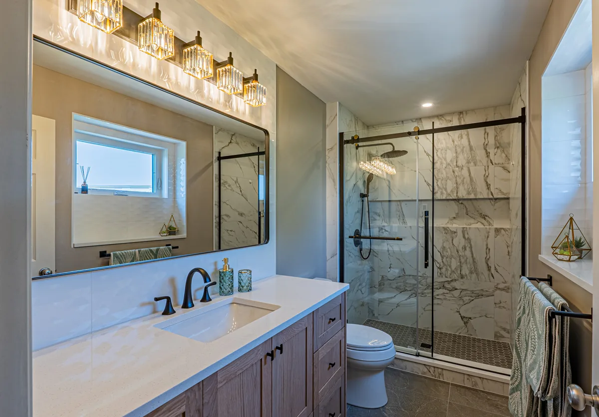 Ensuite with a wood-grain vanity under crystal sconces and a marble-tiled walk-in shower behind glass