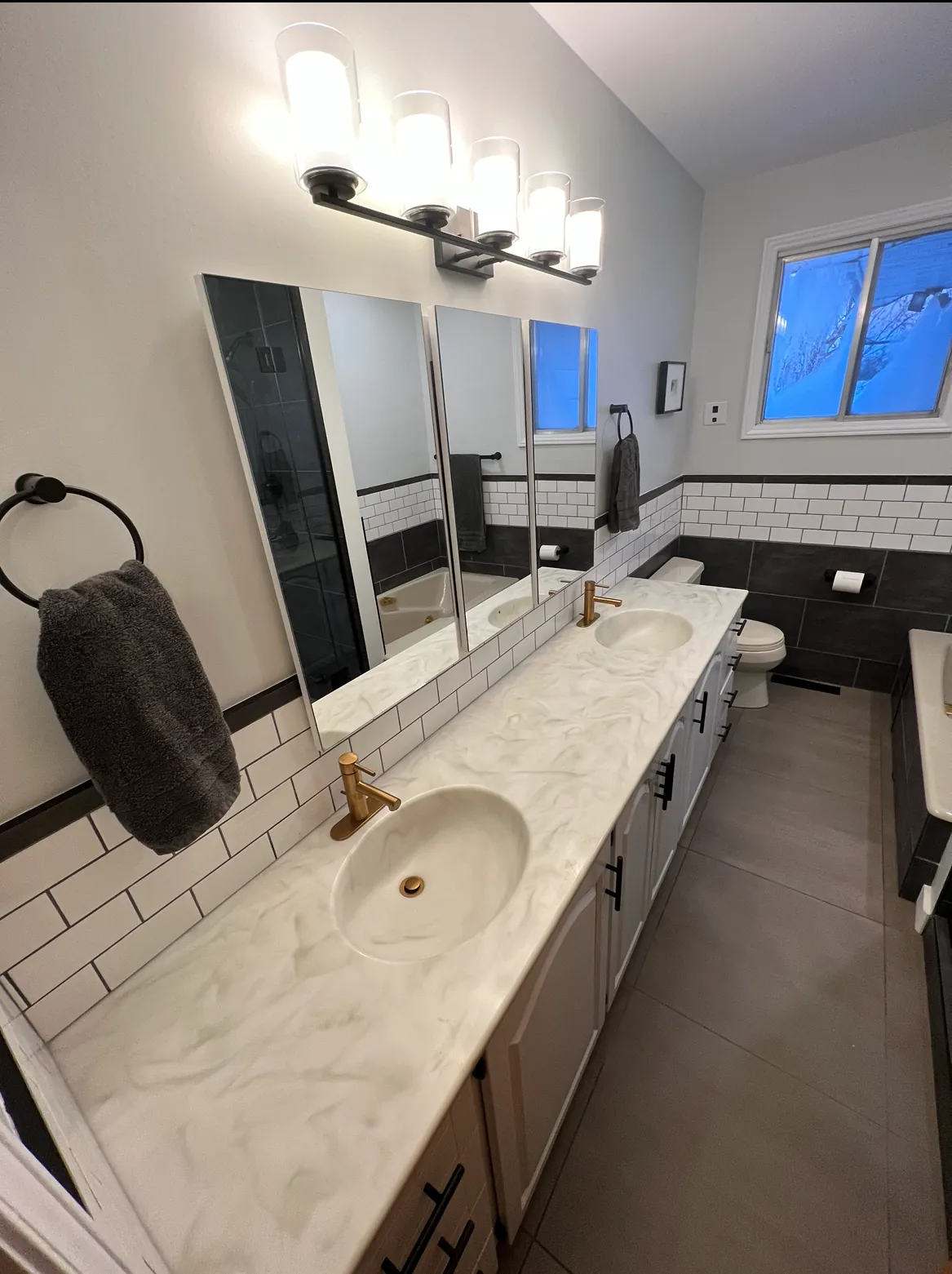 Double marble-topped vanity with gold taps, opposite a black-framed steam shower