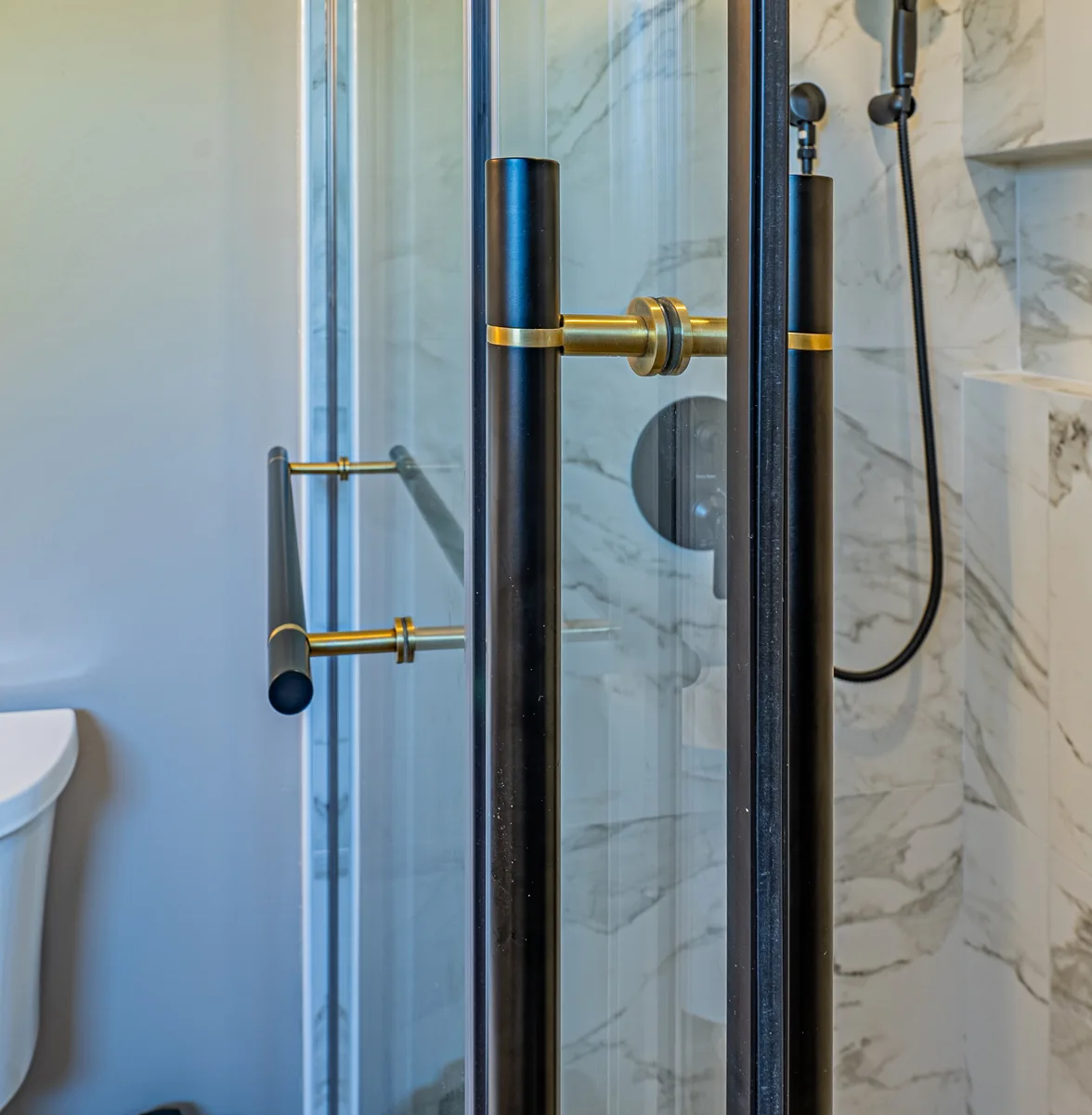 The ensuite's frameless glass shower door with a brass pull against the veined tile