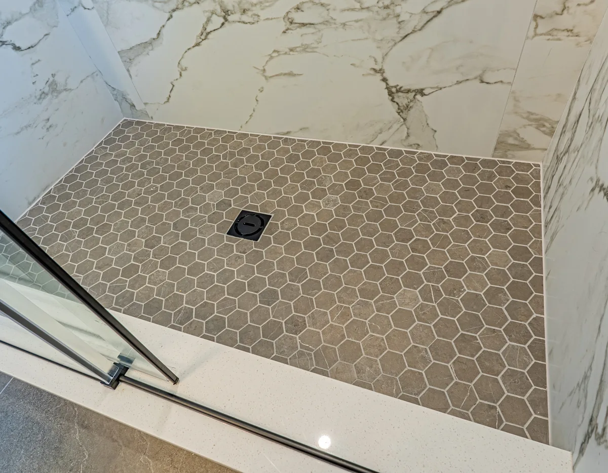 Hex tile shower floor meeting the slab-tiled walls