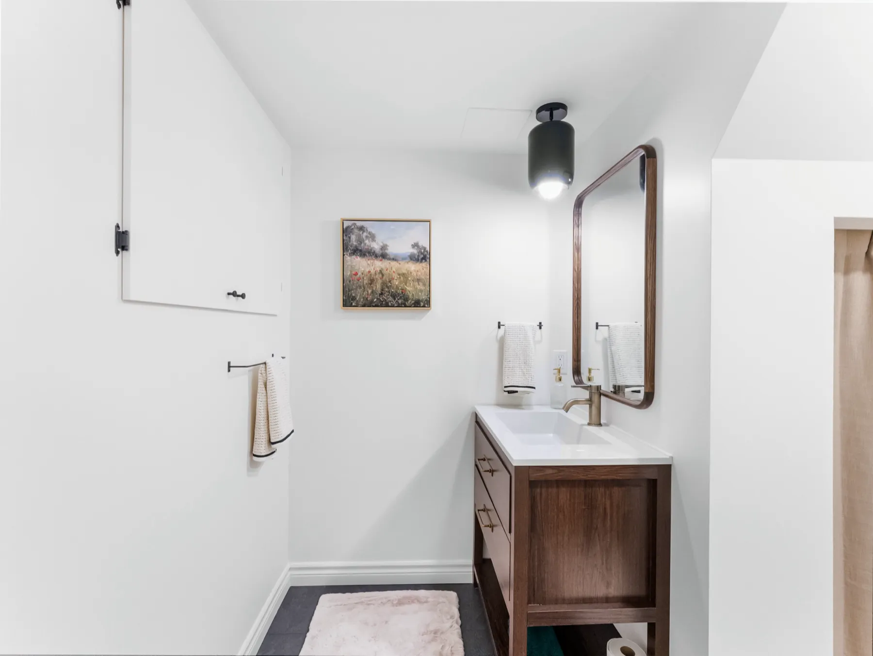 Small bathroom under a sloped ceiling, with a walnut open-shelf vanity and a rounded copper-framed mirror