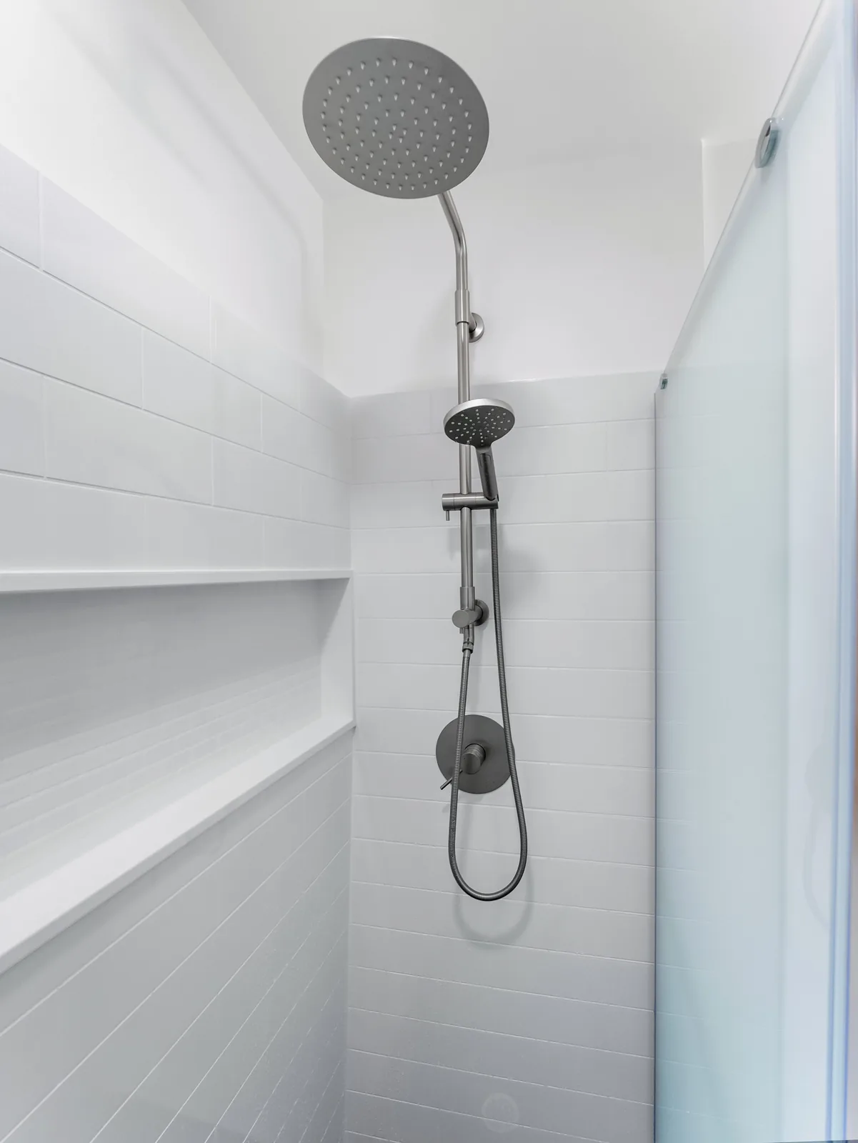 Corner shelf and hand shower set into the panelled shower wall