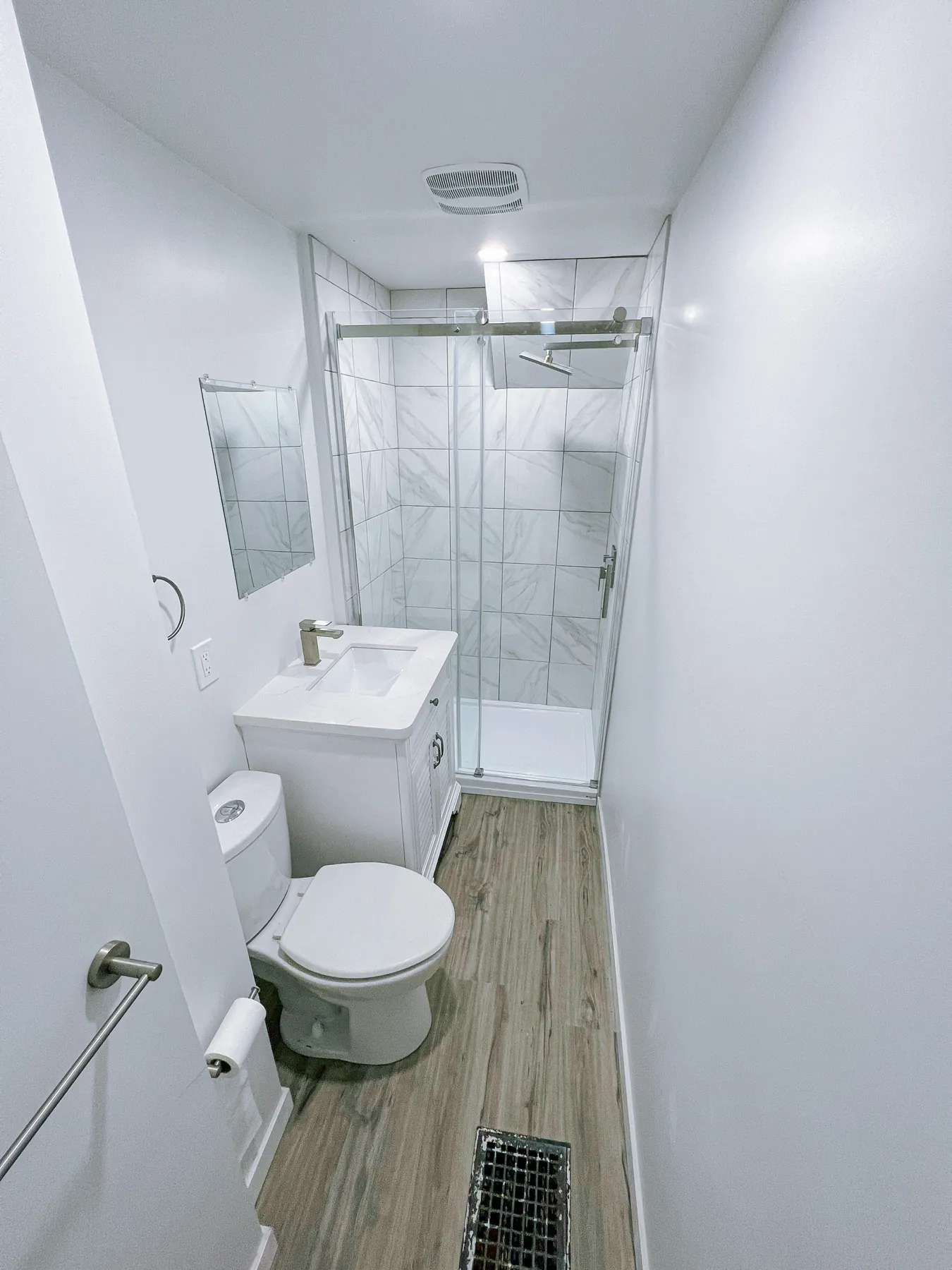 Compact bathroom in white, with a marble-look shower and a wood-look plank floor