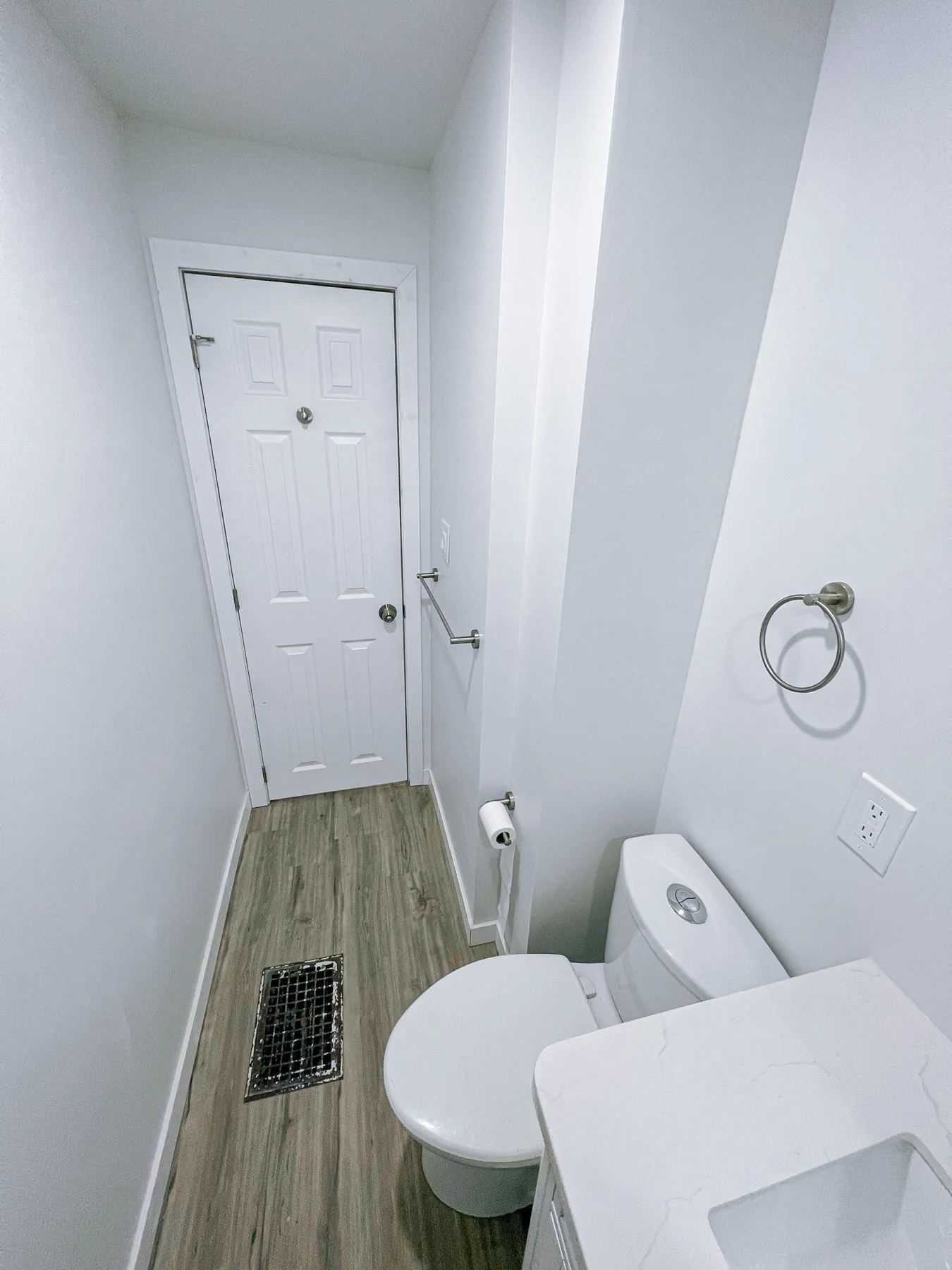 Toilet and the door end of the room, plank floor underfoot