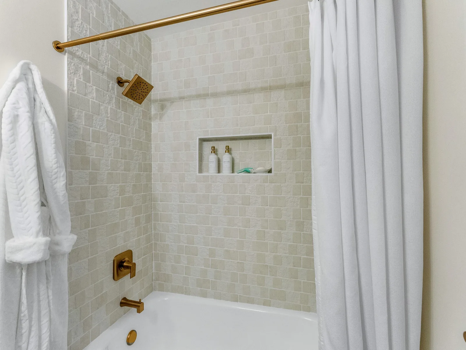 Robe and curtain at the tub, brass shower fittings on the tiled wall