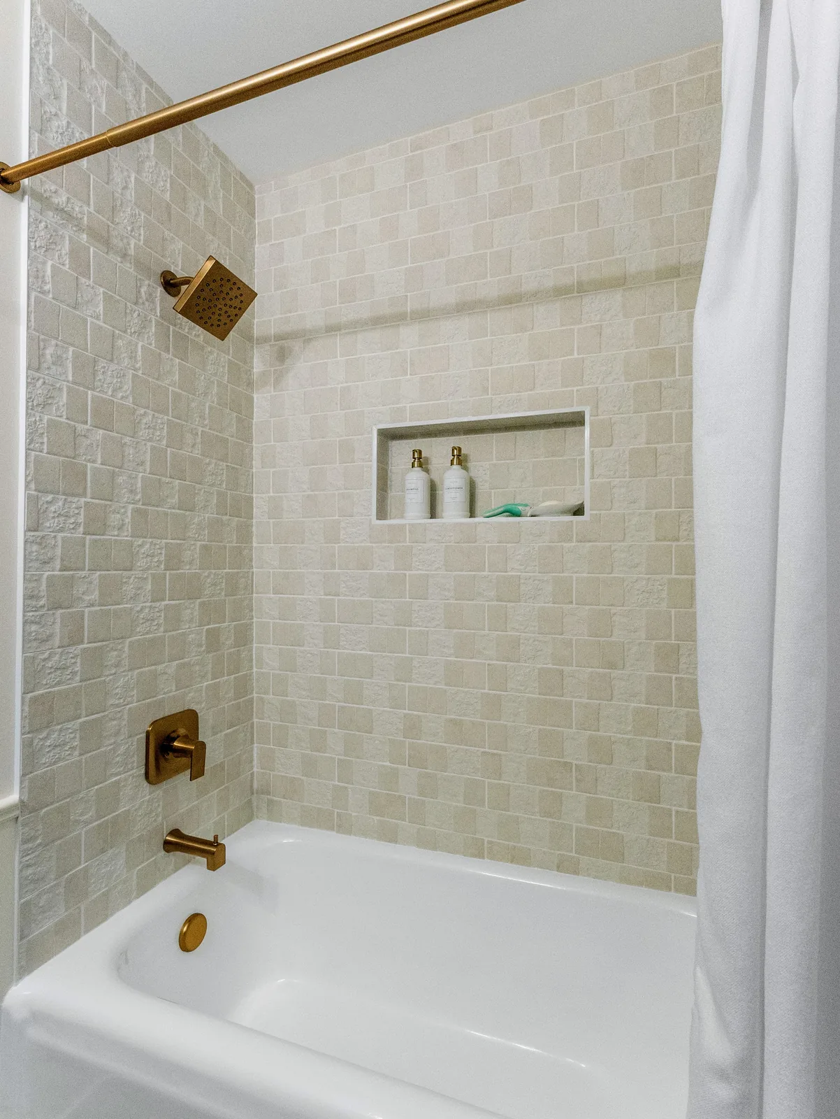 Brass tub filler and shower rail against the white tiled wall