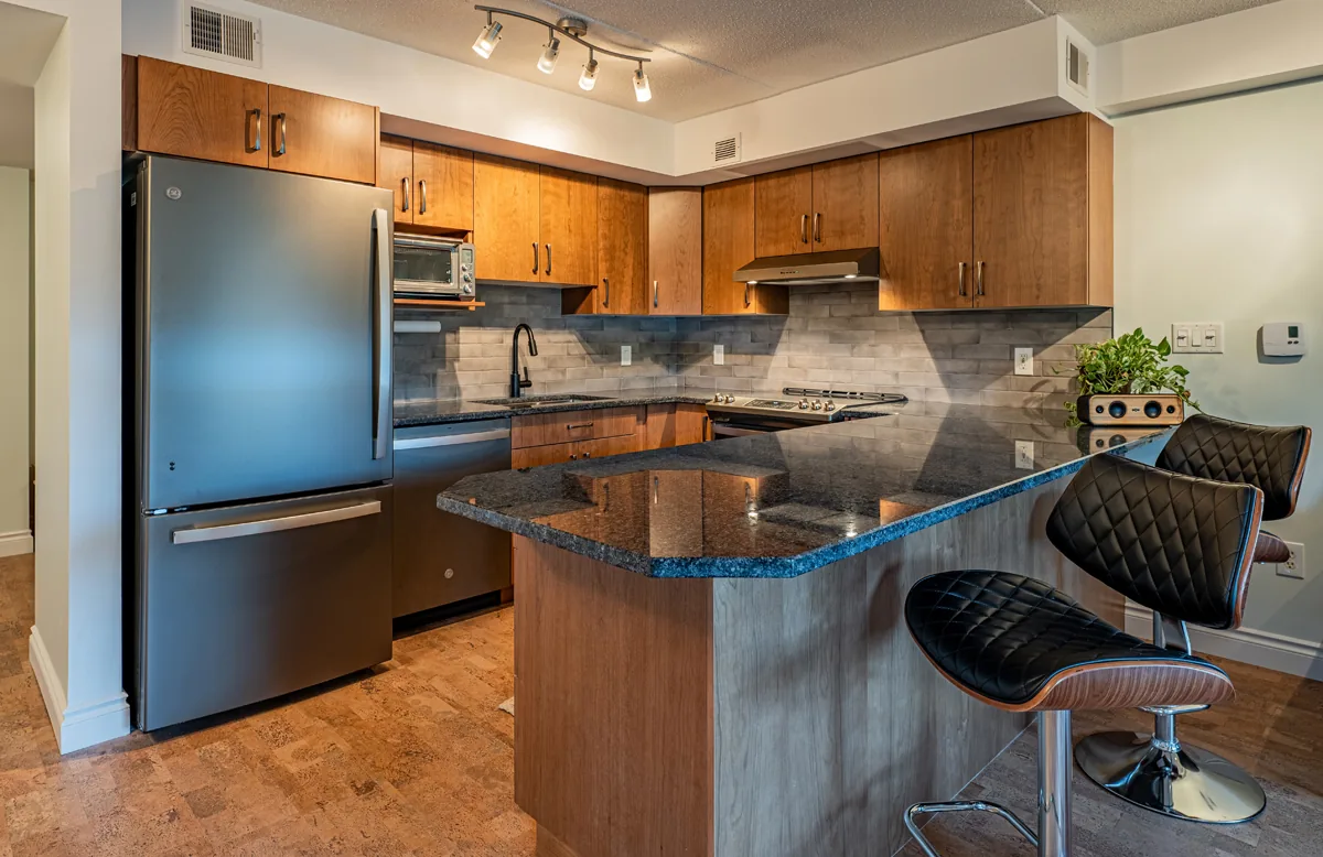 Condo kitchen in cherry cabinetry with a granite peninsula, bar stools and stainless appliances