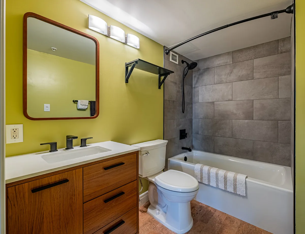 Condo bathroom with a wood vanity, framed mirror and a tiled tub-shower