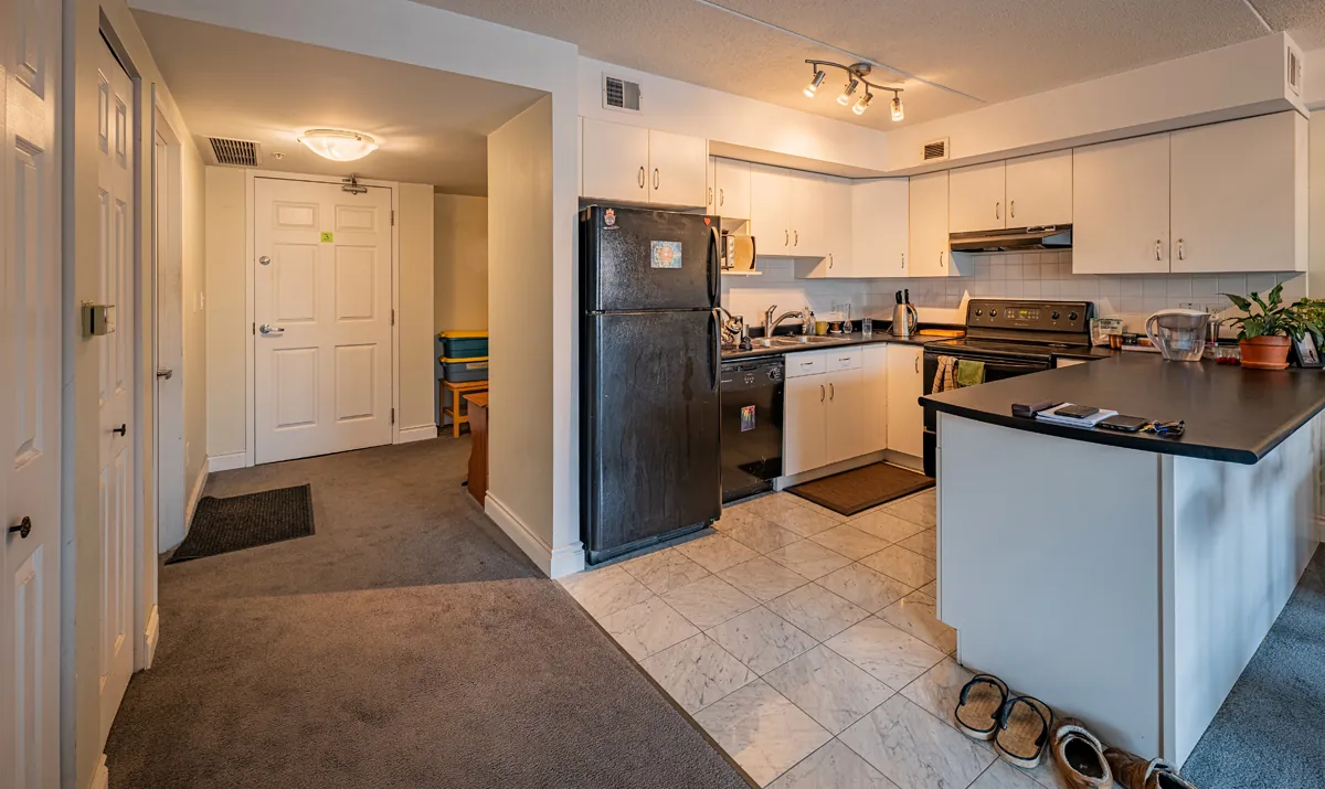 Before: the kitchen in white cabinets with black appliances, tile underfoot and carpet beyond