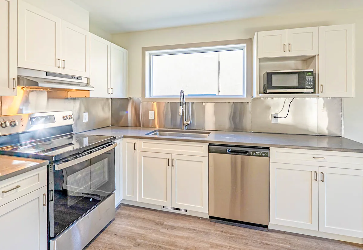 Range and sink run under the window, stainless backsplash along the counter