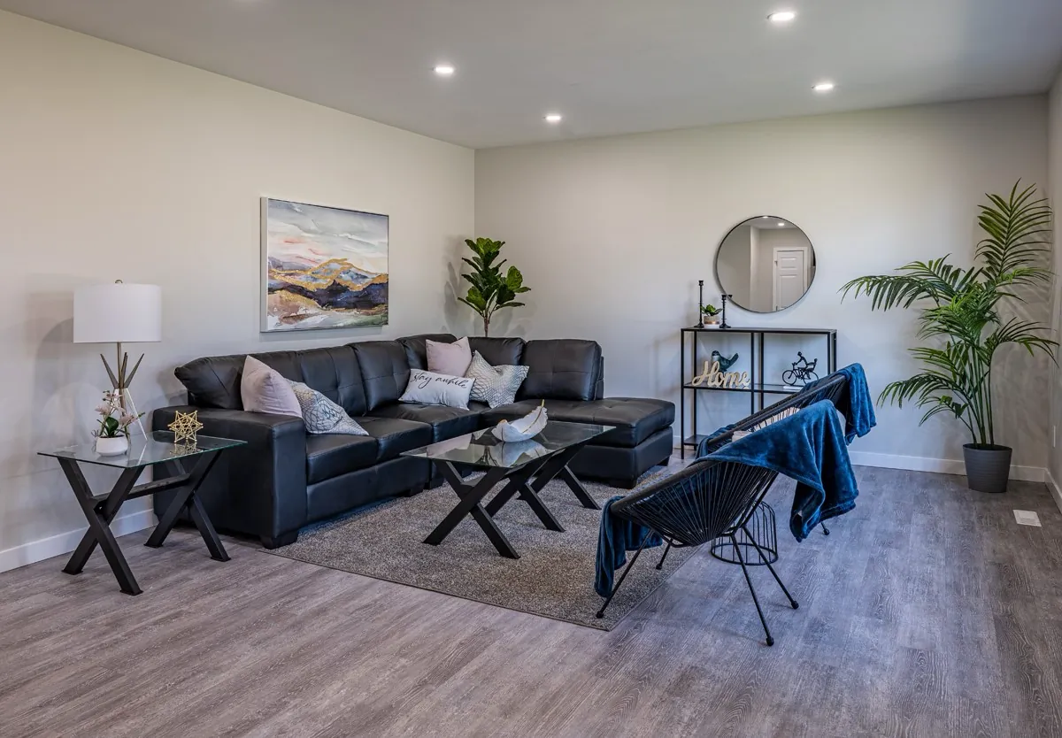 Living room of a full-home remodel, staged at handover — dark sectional, wide-plank floor and recessed lighting