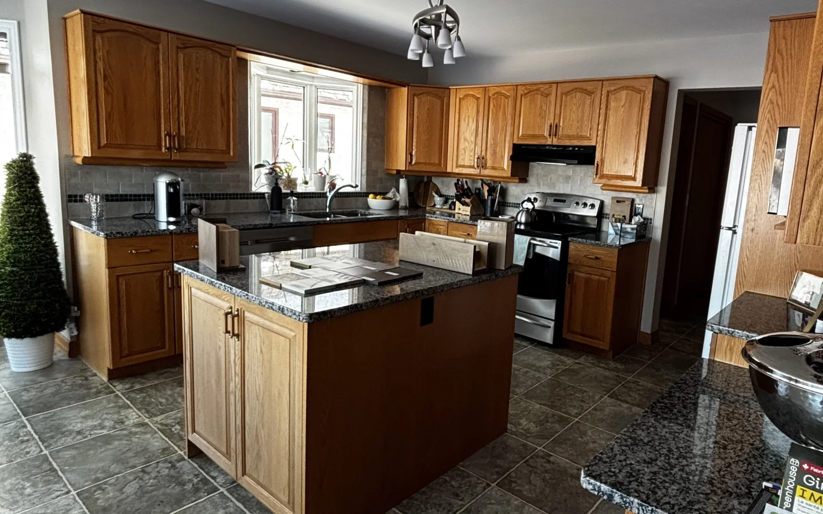 Before — the original kitchen with arched golden-oak cabinets, speckled granite counters, a tile backsplash and dark tile floor