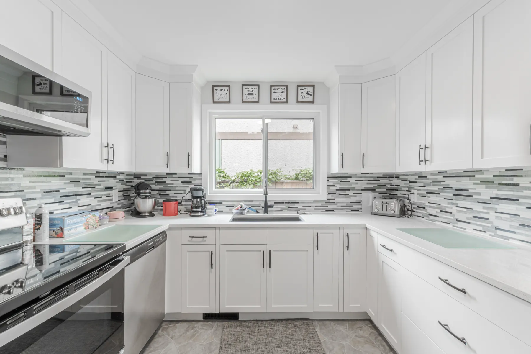 White kitchen with a linear glass mosaic backsplash and a window over the sink