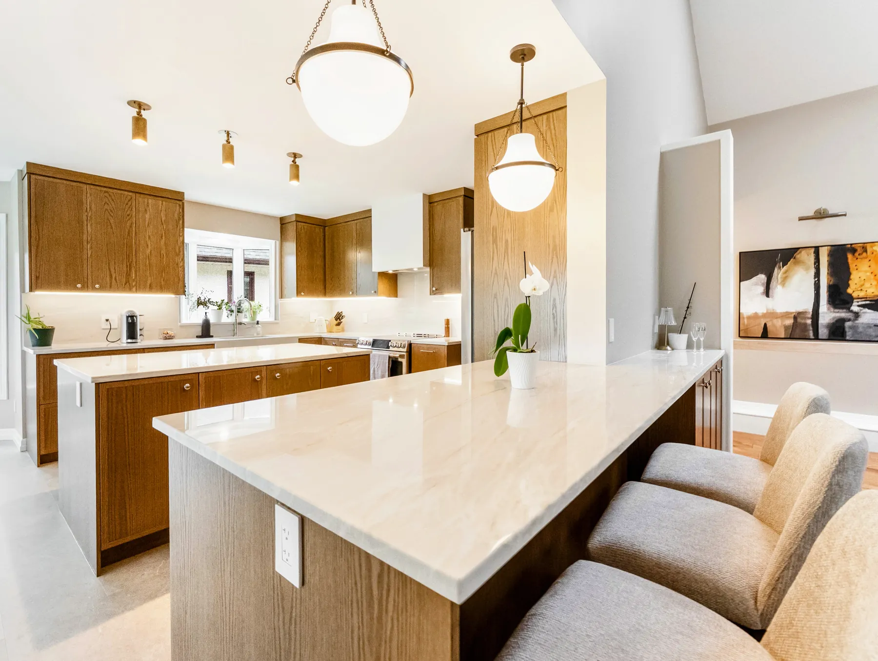 White-oak kitchen bar counter under two brass-and-glass pendants, vaulted ceiling above