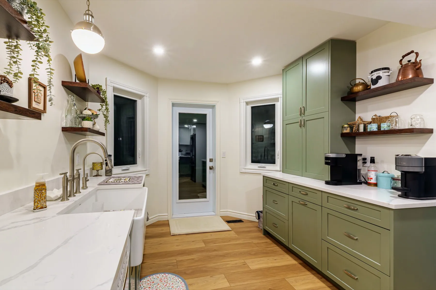 Farmhouse sink and brass tap under walnut floating shelves, a tall olive pantry by the back door