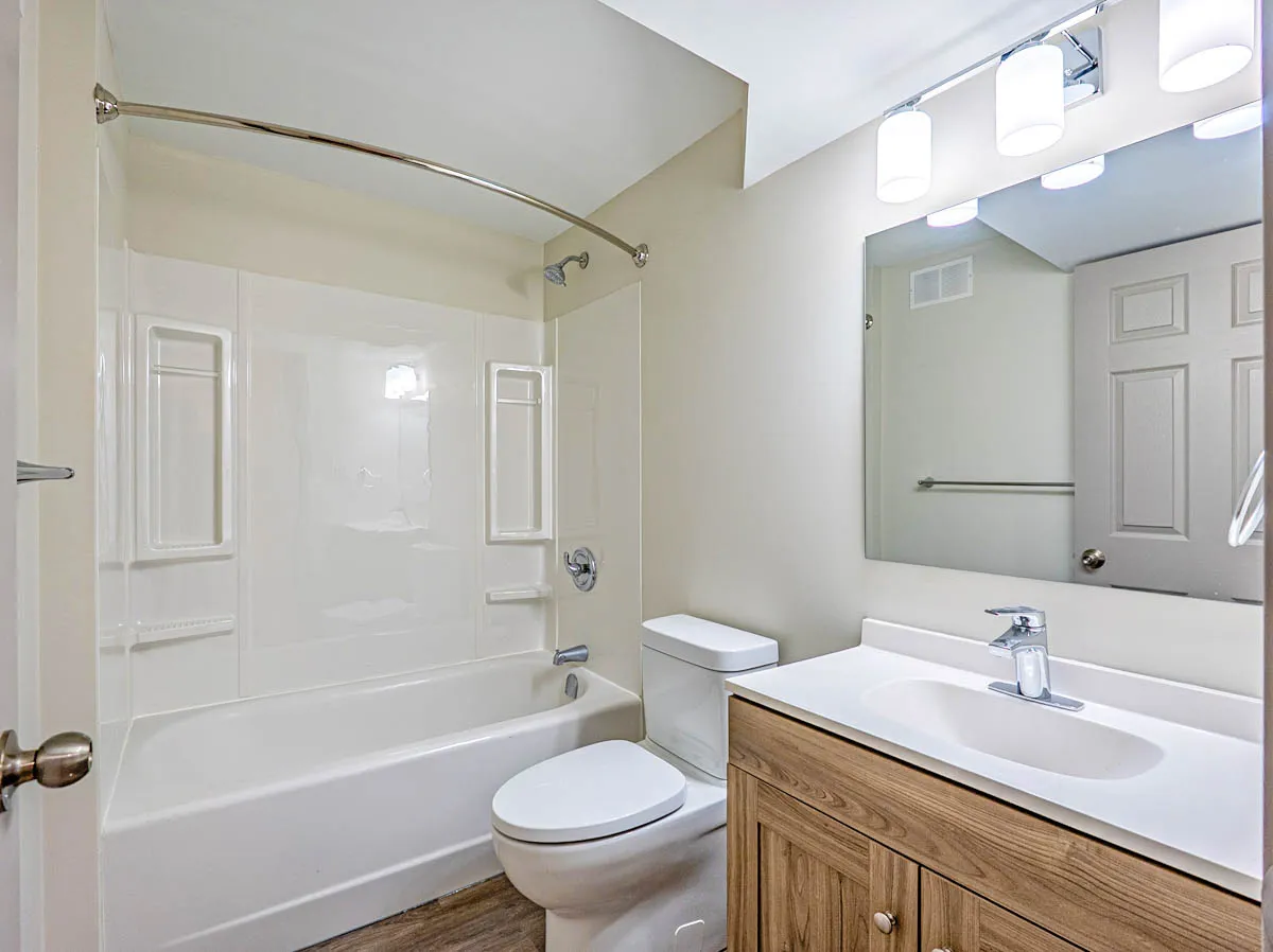 Bathroom with a tub-shower, wood-front vanity and a light bar over the mirror