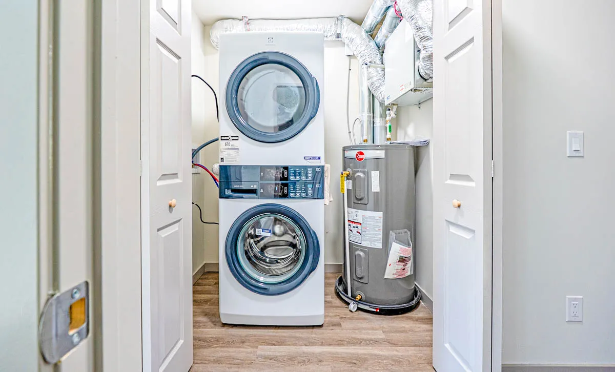 A stacked washer and dryer beside the water heater