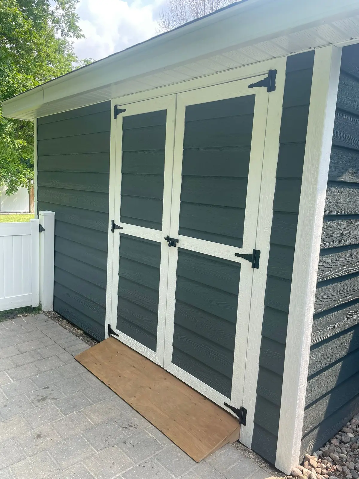 Backyard shed clad in dark teal lap siding, with braced double doors on black strap hinges