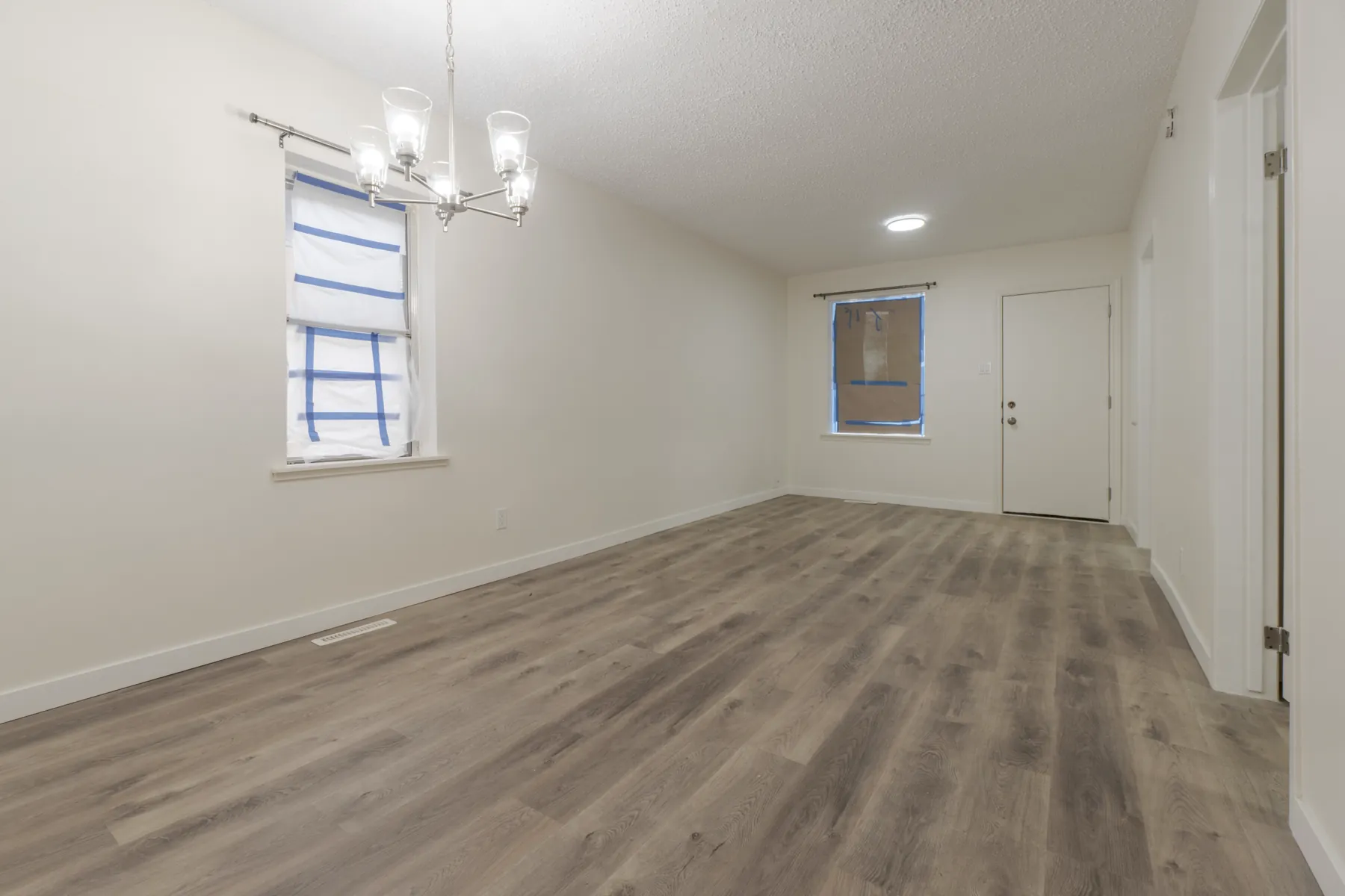 Open living and dining space under a chandelier, vinyl plank throughout