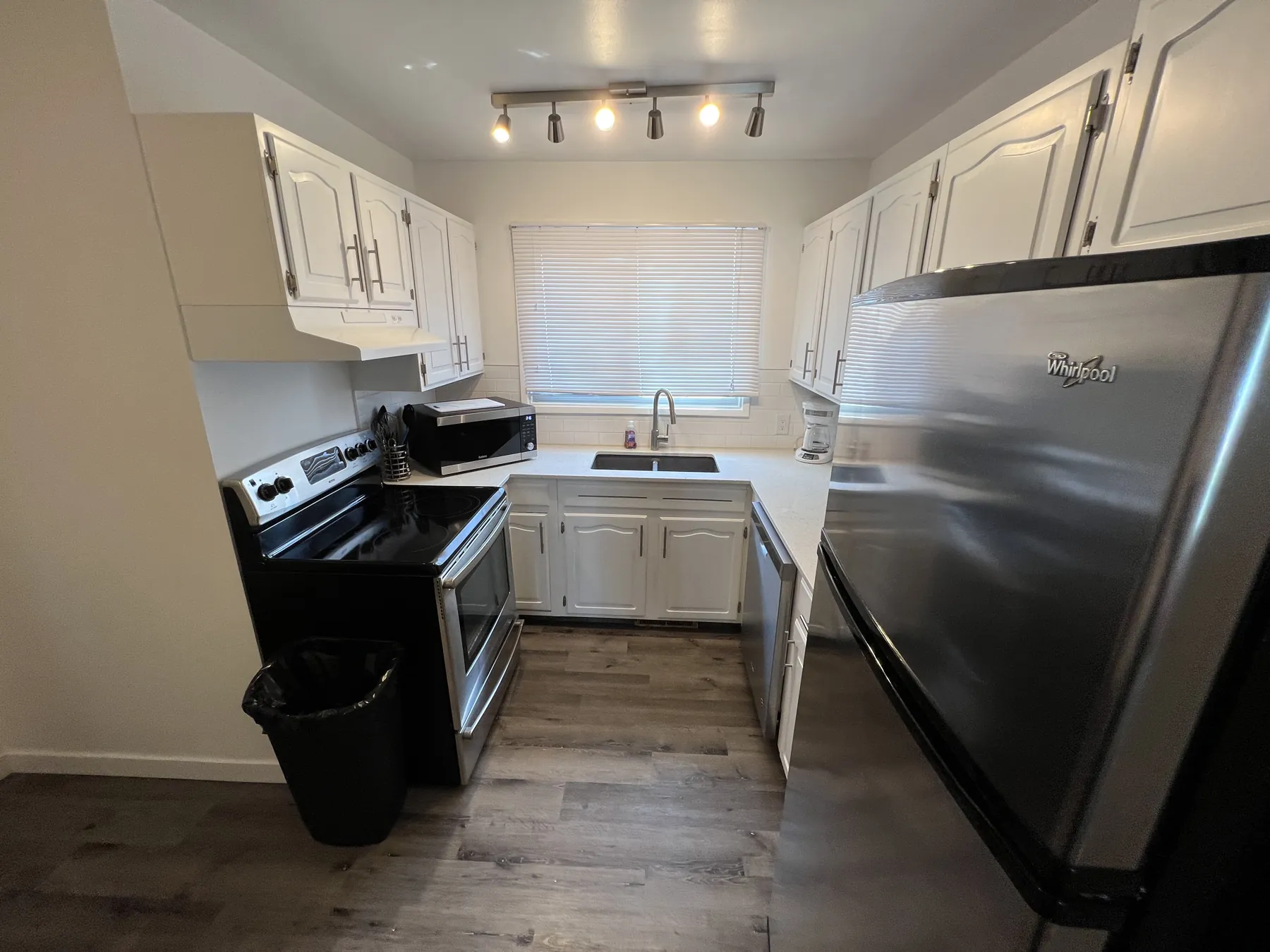 Suite kitchen in white cabinetry with stainless appliances under track lighting
