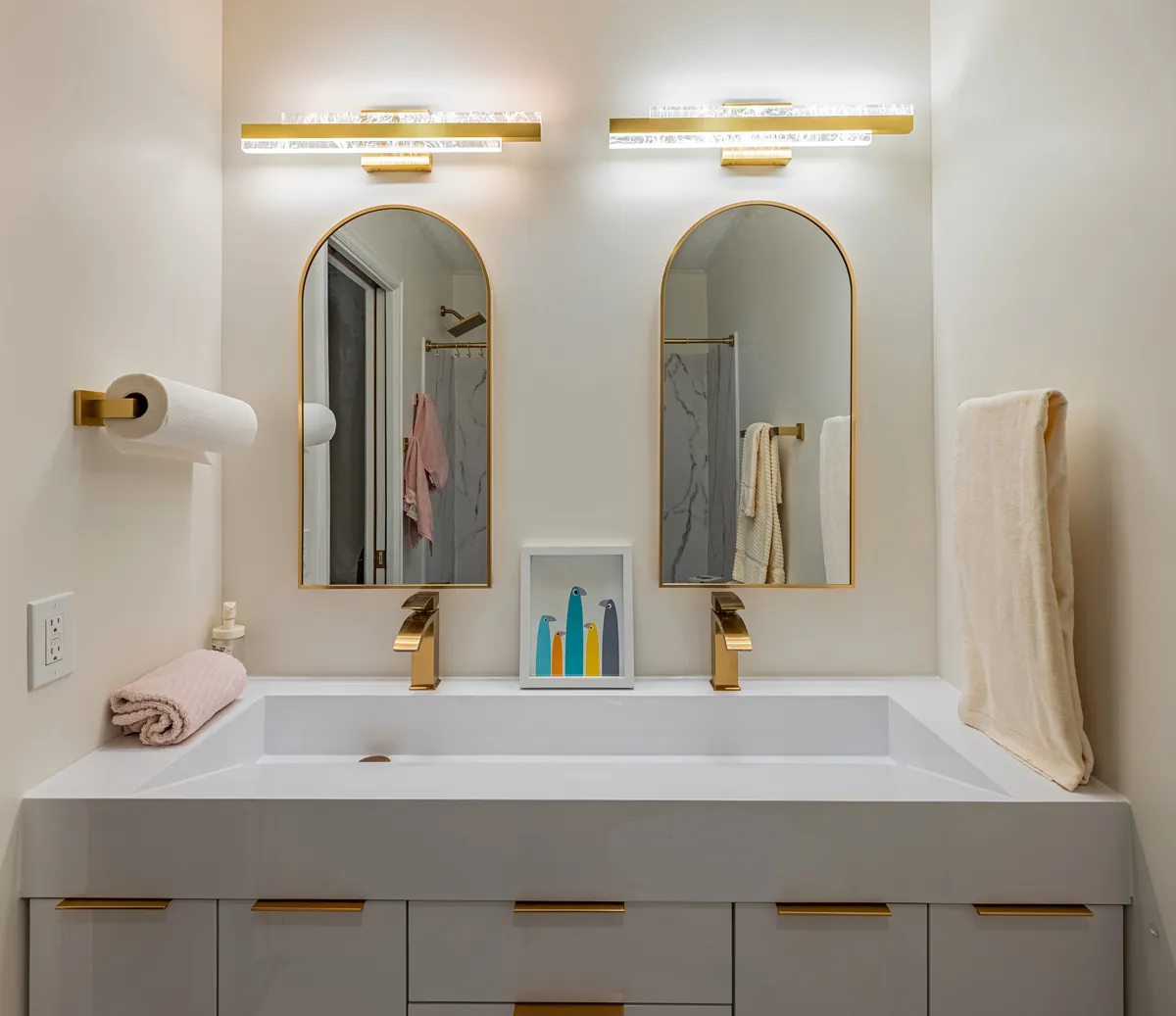 First bathroom: a wide trough sink under twin arched mirrors, gold fixtures