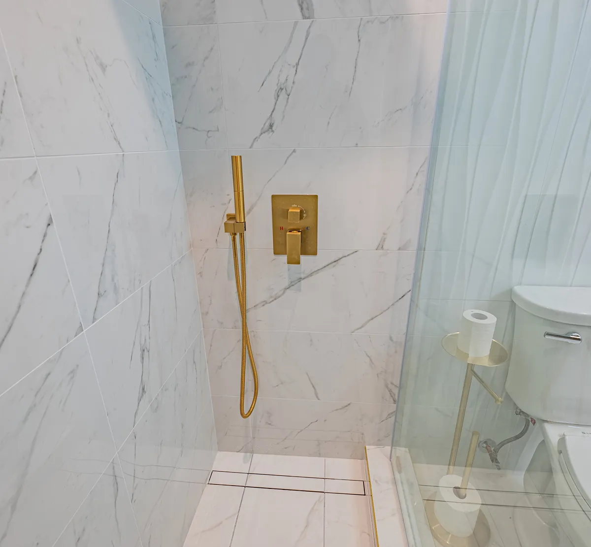 Inside the third bathroom's shower, a gold hand shower on the veined tile