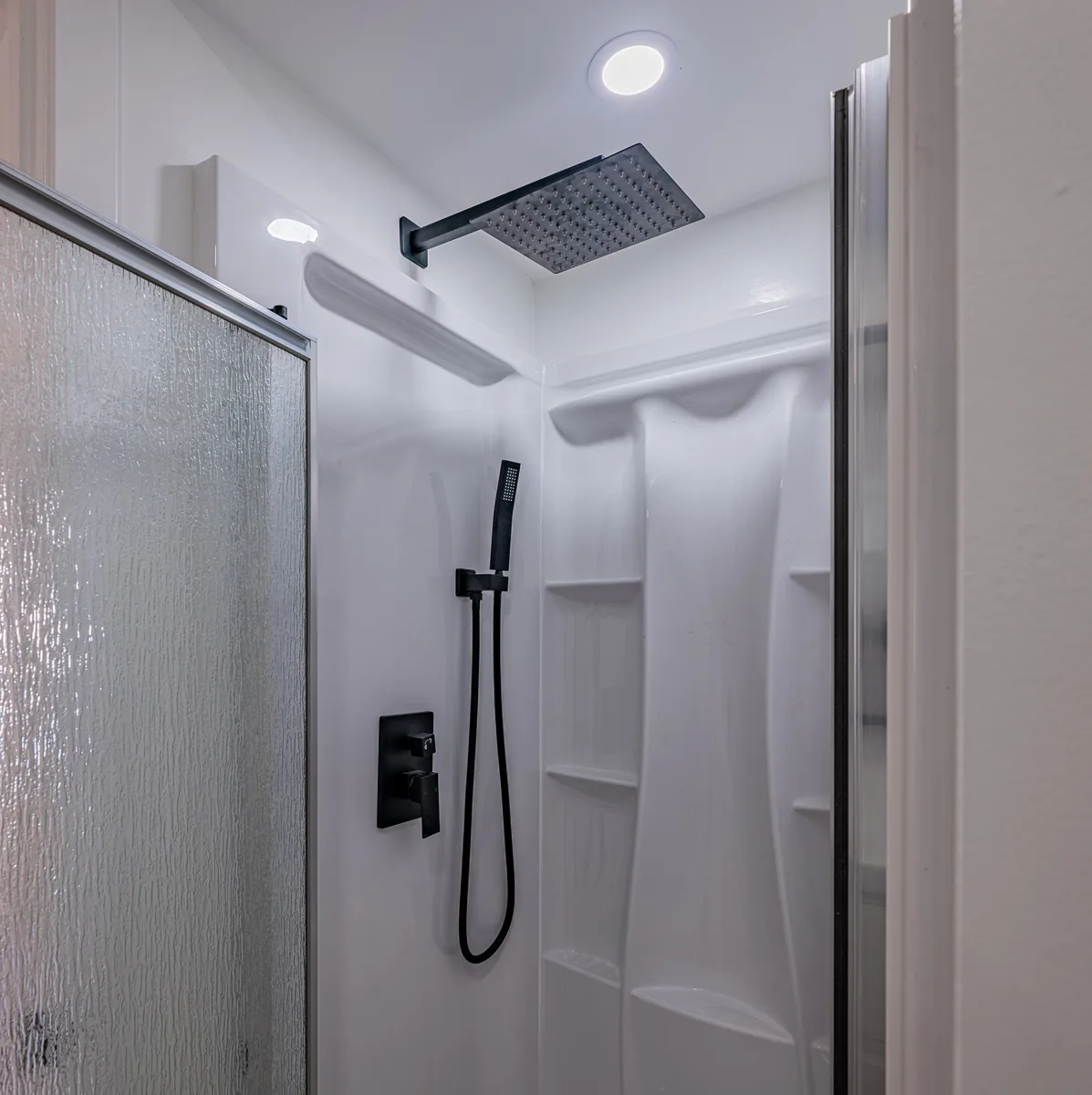 Walk-in shower with a black rain head and a sliding glass door