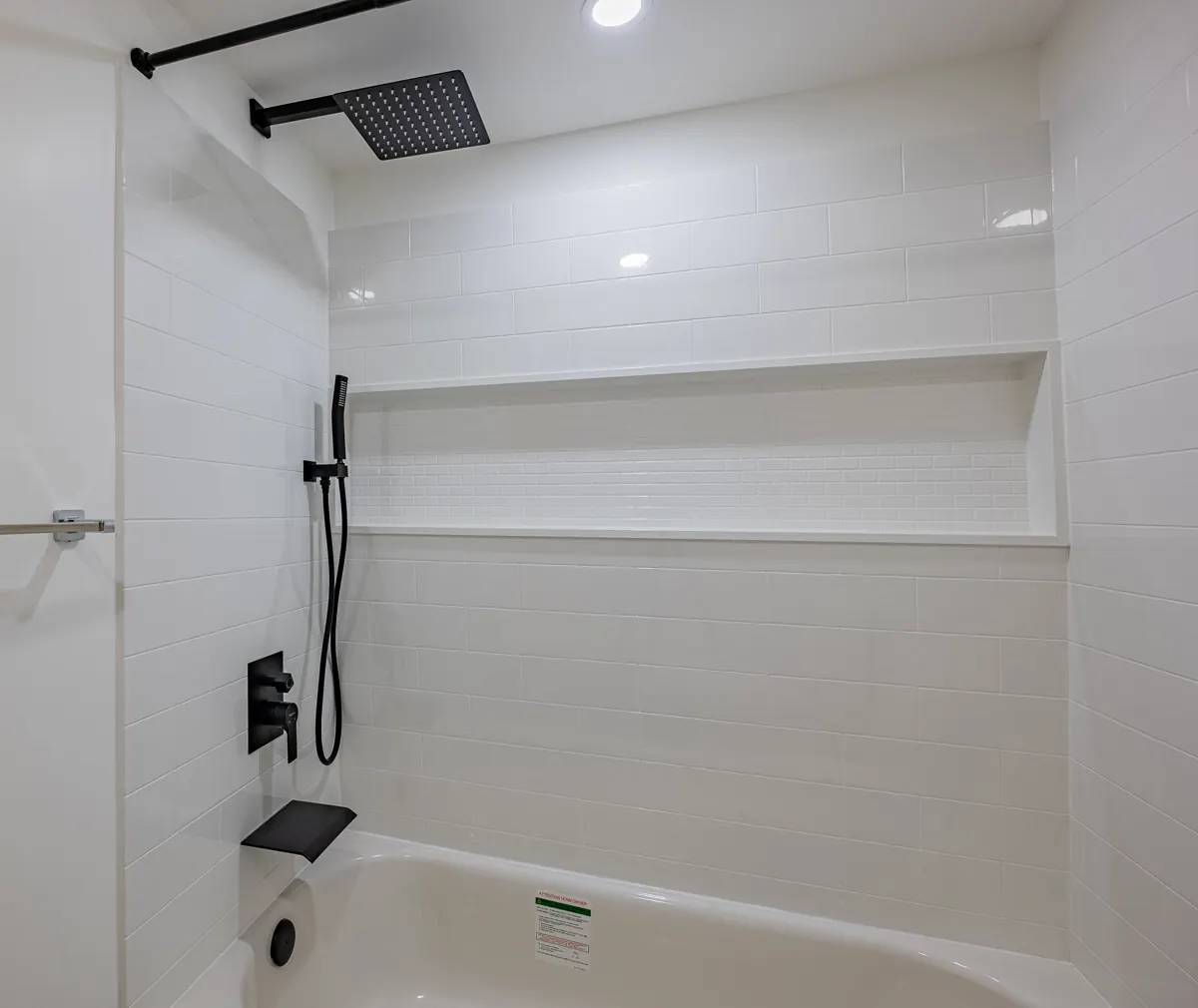 Tub and shower in white tile, a long niche and a black rain head above
