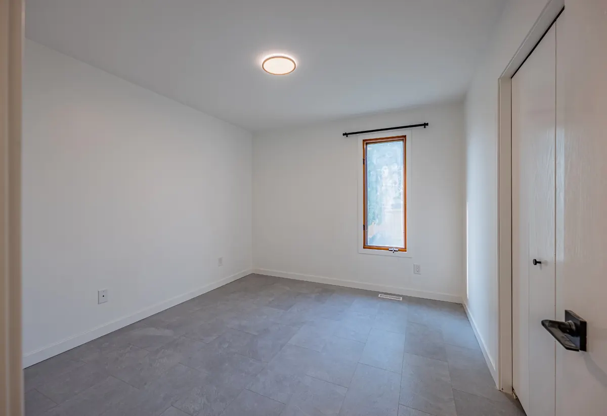 A bedroom with tile flooring and a tall wood-framed window