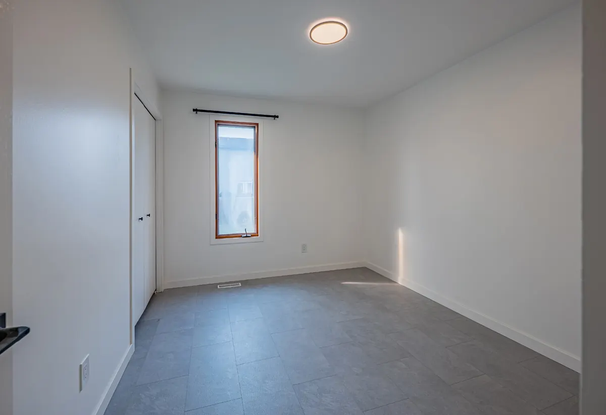 A smaller bedroom with a single tall window